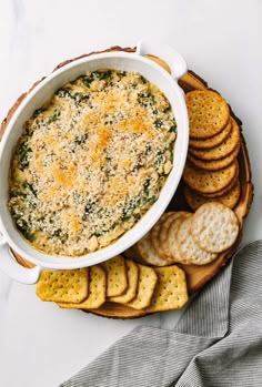 a bowl of spinach dip surrounded by crackers on a platter with cheese