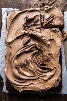 a chocolate cake with frosting on it sitting on a piece of paper next to a knife