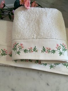 two white towels sitting on top of a counter next to pink flowers and greenery