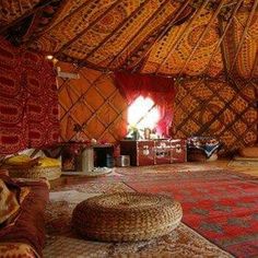 the inside of a yurt with colorful rugs and pillows on the floor in front of it