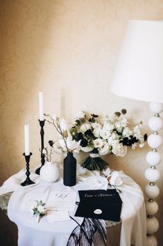 a table topped with white flowers and candles next to a vase filled with flowers on top of a table