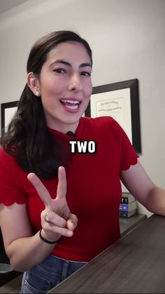 a woman in a red shirt is giving the peace sign with her hand and two fingers