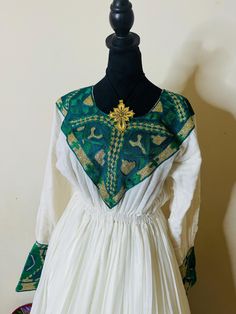 Ethiopian and Eritrean traditional dress(habesha kemis) that appears to be of Ethiopian origin. It features a long white skirt with green and gold intricate designs around the bottom and on the chest area. The dress is paired . This style of dress is commonly referred to as a "Habesha Kemis," a traditional Ethiopian and Eritrean garment often worn during cultural celebrations or special occasions. The embroidery and colors are typical of this style, which is known for its elegant and flowing design. Long White Skirt, Habesha Kemis, White Long Skirt, Cultural Celebration, White Skirt, Traditional Dress, Silver Spring, Intricate Designs, White Skirts