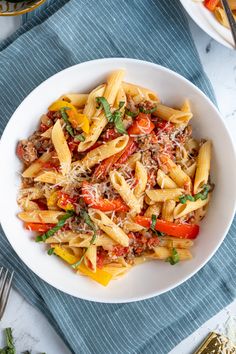 a white bowl filled with pasta and vegetables on top of a blue towel next to silverware