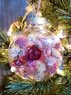 a glass ornament with flowers in it hanging from a christmas tree, decorated with pine needles