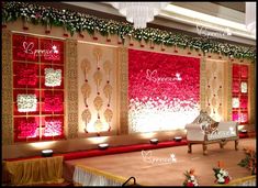 a stage set up for a wedding ceremony with red and white flowers on the wall