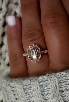 a woman's hand with a ring on her finger and a sweater in the background