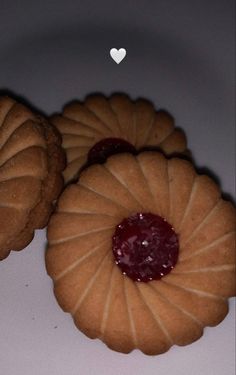 three cookies with jam on them sitting next to each other in front of a white heart