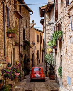 an old red car parked in the middle of a cobblestone street with potted plants