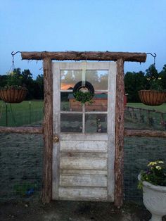 an old wooden door with a wreath on it and some flowers in the yard next to it