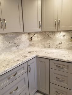 a kitchen with white cabinets and marble counter tops