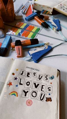 an open book with the words jesus loves you written on it next to markers and crayons