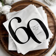 four napkins with the number sixty on them sitting on a wooden plate next to flowers