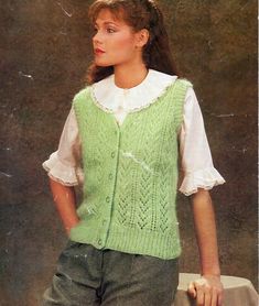 a woman wearing a green sweater vest and white shirt standing in front of a wall