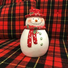 a white snowman sitting on top of a red and black plaid couch next to a pillow