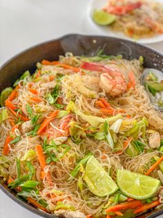 a pan filled with noodles and vegetables on top of a white tablecloth next to two plates of food