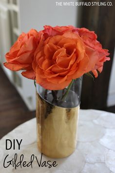 an orange rose in a gold vase sitting on a table with the words diy gilded vase