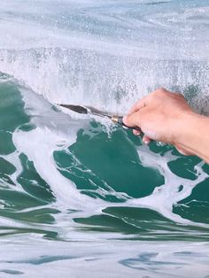 a person is holding a paintbrush in their left hand while painting a wave on the water