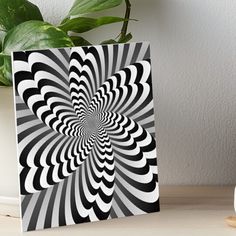 an abstract black and white spiral design art board on a table next to a potted plant