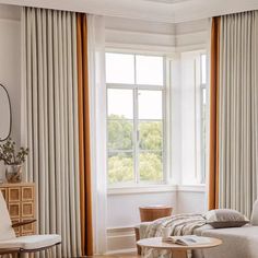 a living room filled with furniture and a large window covered in draping next to a wooden coffee table