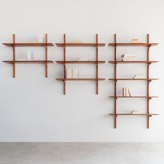 three wooden shelves with books on them against a white wall in an empty room,