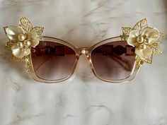 Enjoy these fabulous statement sunglasses while out running errands or at your next big event! This fabulous pair of sunglasses is embellished with large flowers with petal centers, gold leaves, and other fun touches of gold charms, such as a bee, and more. ♥ Handmade with quality and care for maximum moxie ♥ (If you would like to (further) customize this, or your own pair of sunglasses, message me!) #handmadesunglasses #customizedsunglasses #rhinestonesunglasses #blingsunglasses #bridal #bridal Glamorous Gold Party Sunglasses, Glamorous Gold Sunglasses For Party, Glamorous Gold Sunglasses For Summer, Elegant White Sunglasses For Wedding, Elegant White Wedding Sunglasses, Elegant Gold Sunglasses For Summer, Elegant Gold Sunglasses For Spring, Elegant Gold Sunglasses, Elegant Evening Sunglasses For Spring