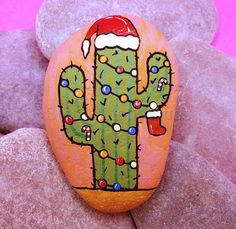 a painted rock with a christmas cactus on it, surrounded by rocks and stones in the background