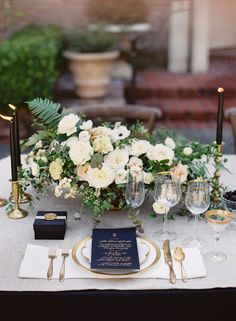 an elegant table setting with white flowers and black napkins, gold rimmed glasses and candles