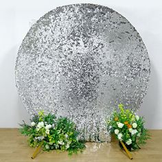 two flower arrangements sit in front of a large mirror with flowers on the bottom and sides