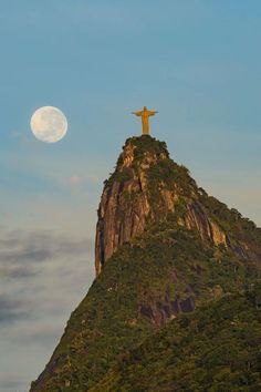 a large statue on top of a mountain with a moon in the sky behind it