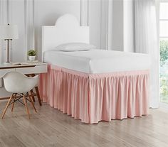 a white bed with pink ruffled bedskirt next to a desk and chair