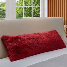 a red fluffy pillow sitting on top of a white couch next to a windowsill