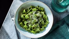 a white bowl filled with green pasta on top of a table next to a fork