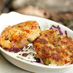 two crab cakes in a white bowl with coleslaw and slaw on the side