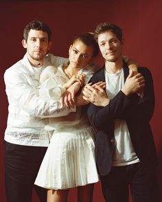 three people standing next to each other in front of a red wall with their arms around one another