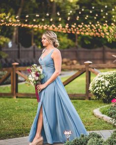 a woman in a blue dress holding a bouquet and standing on a sidewalk near flowers