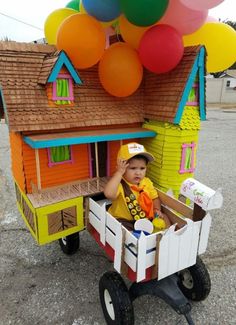 a small child in a toy wagon with balloons on the roof and a house made out of cardboard