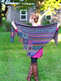 a woman holding up a colorful shawl in the grass