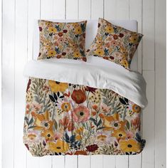 a bed with floral comforter and pillows on top of it, against a white wall