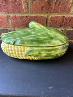 a corn cob shaped bowl sitting on top of a black table next to a brick wall