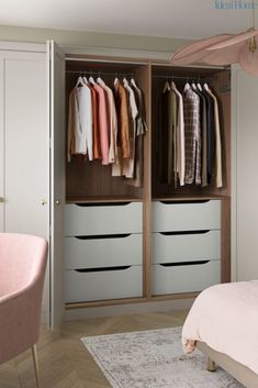 an open closet with clothes hanging on the doors and two pink chairs in front of it