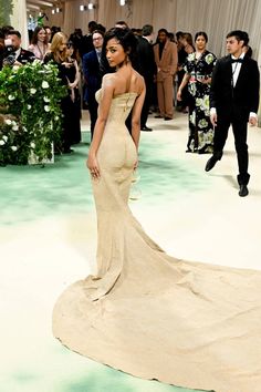 a woman in a long dress standing on a green carpet with people looking at her