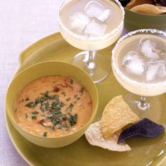 there is a bowl of dip and chips on the plate next to two wine glasses