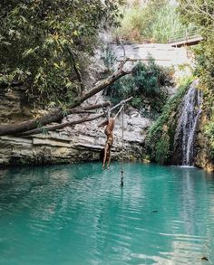 a man hanging from a rope in the middle of a body of water with a waterfall behind him