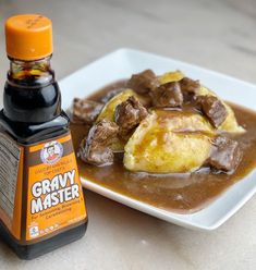 a white plate topped with meat and gravy next to a bottle of sauce