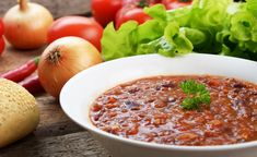 a white bowl filled with chili next to lettuce and tomatoes