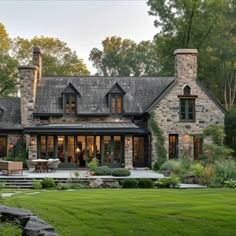 a large stone house surrounded by lush green grass and trees in the background, with an outdoor dining area next to it