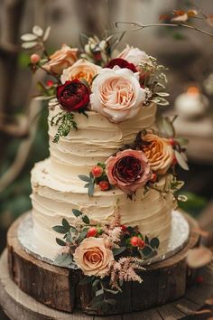 a three tiered cake with flowers and greenery on top is sitting on a wooden stand