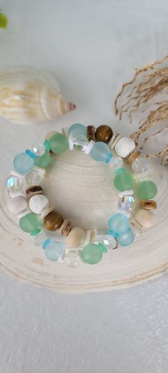 a bracelet made with sea glass and seashells on a white plate next to shells