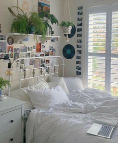 a bed with white sheets and pillows in a bedroom next to a window filled with plants